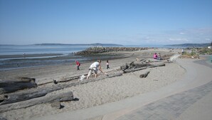 A beach with a paved walkway, rocky shoreline, and people engaging in various activities.