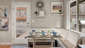 A dining area with a wooden table set for four, a clock, and framed artwork on the wall.