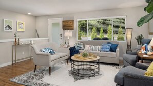 A living room with a sofa, armchairs, a coffee table, and a large window with blinds.