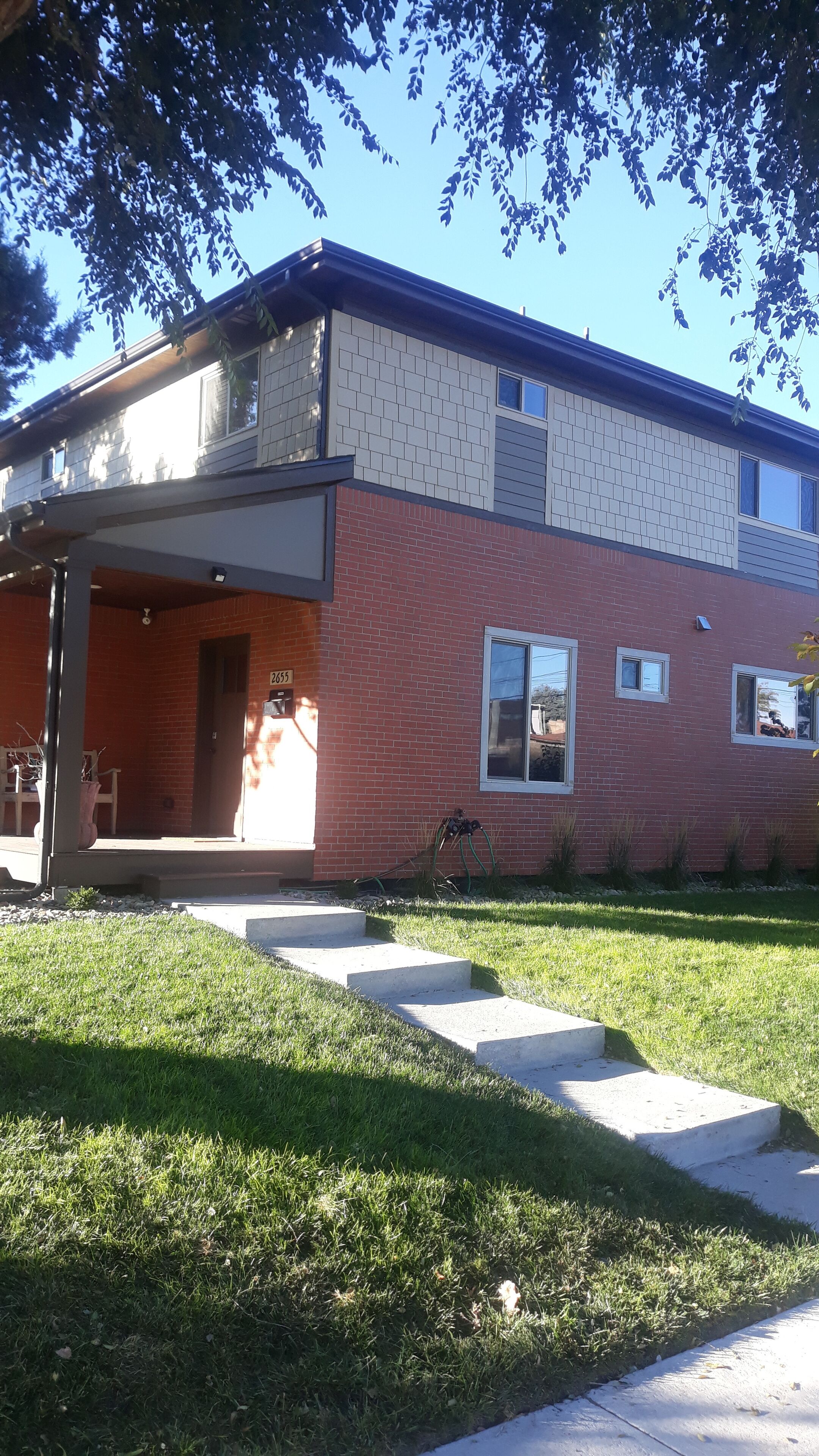 A two-story building with a brick facade, a covered front porch, and a small front yard.