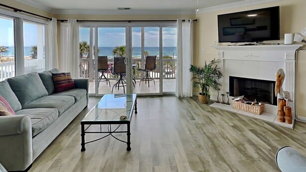 A living room with a sofa, coffee table, TV, fireplace, and a balcony with a view of the ocean. - Oceanfront condo w. beach access + balcony views. (Tybee Island)