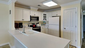 A kitchen with white cabinets, a stainless steel sink, a microwave, a stove, and a refrigerator. - Oceanfront condo w. beach access + balcony views. (Tybee Island)