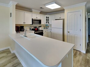 A kitchen with white cabinets, a stainless steel sink, a microwave, a stove, and a refrigerator.