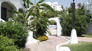 A pathway leading to a white building with arches, surrounded by lush greenery and a lamp post. - Albatros Beach Club (Benalmádena)