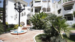 A courtyard with a fountain, palm trees, and a white building with balconies. - Albatros Beach Club (Benalmádena)