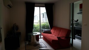A modern living room with a red sofa, a glass table, and a view of a balcony with greenery.