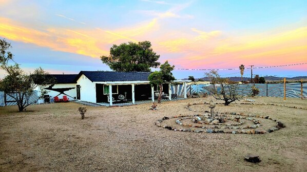 A single-story house with a covered porch, a fenced yard, and a clear sky. - Private stargazing retreat with Firepit/Views/ Spa/King bed (Joshua Tree)