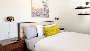A neatly arranged bedroom with a bed, bedside tables, a nightstand, a wall-mounted lamp, and a framed picture. - Private stargazing retreat with Firepit/Views/ Spa/King bed (Joshua Tree)
