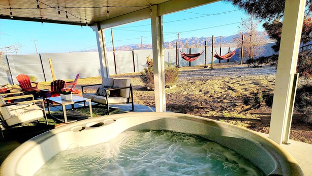 A hot tub with a view of mountains and a patio area with outdoor furniture. - Private stargazing retreat with Firepit/Views/ Spa/King bed (Joshua Tree)