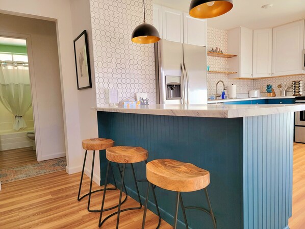 A modern kitchen with a central island, bar stools, a water dispenser, and a sink.