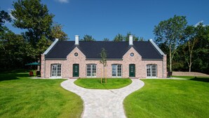 A brick house with a central driveway leading to a front door, surrounded by well-maintained lawns. - Mia - Exclusive vacation home with sauna, fireplace, 4 pers. (Vitzdorf)