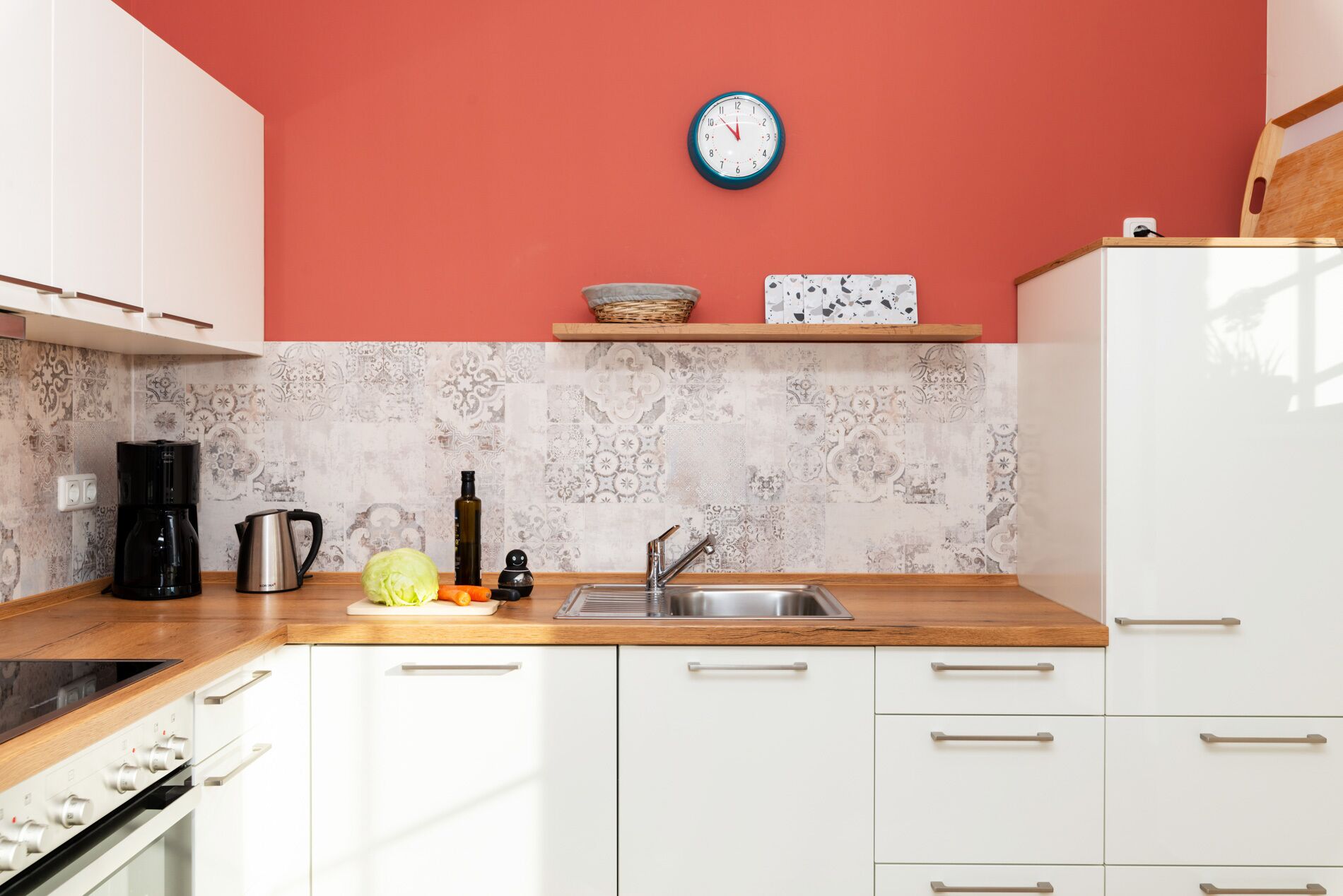 A modern kitchen with white cabinets, a wooden countertop, a sink, and a clock on the wall.