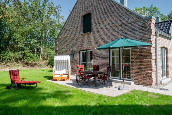 A brick house with a patio area featuring a table and chairs, a covered outdoor seating area, and a lawn. - Mia - Exclusive vacation home with sauna, fireplace, 4 pers. (Vitzdorf)