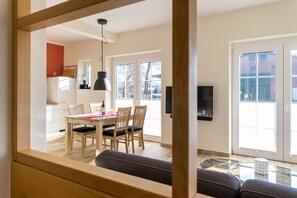 Ett modernt matområde med ett träbord och stolar, en hängande lampa och utsikt över omgivningen genom stora fönster.
