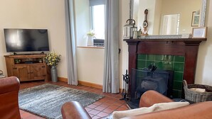 Un soggiorno con camino, divani in pelle, televisore e pavimento piastrellato.