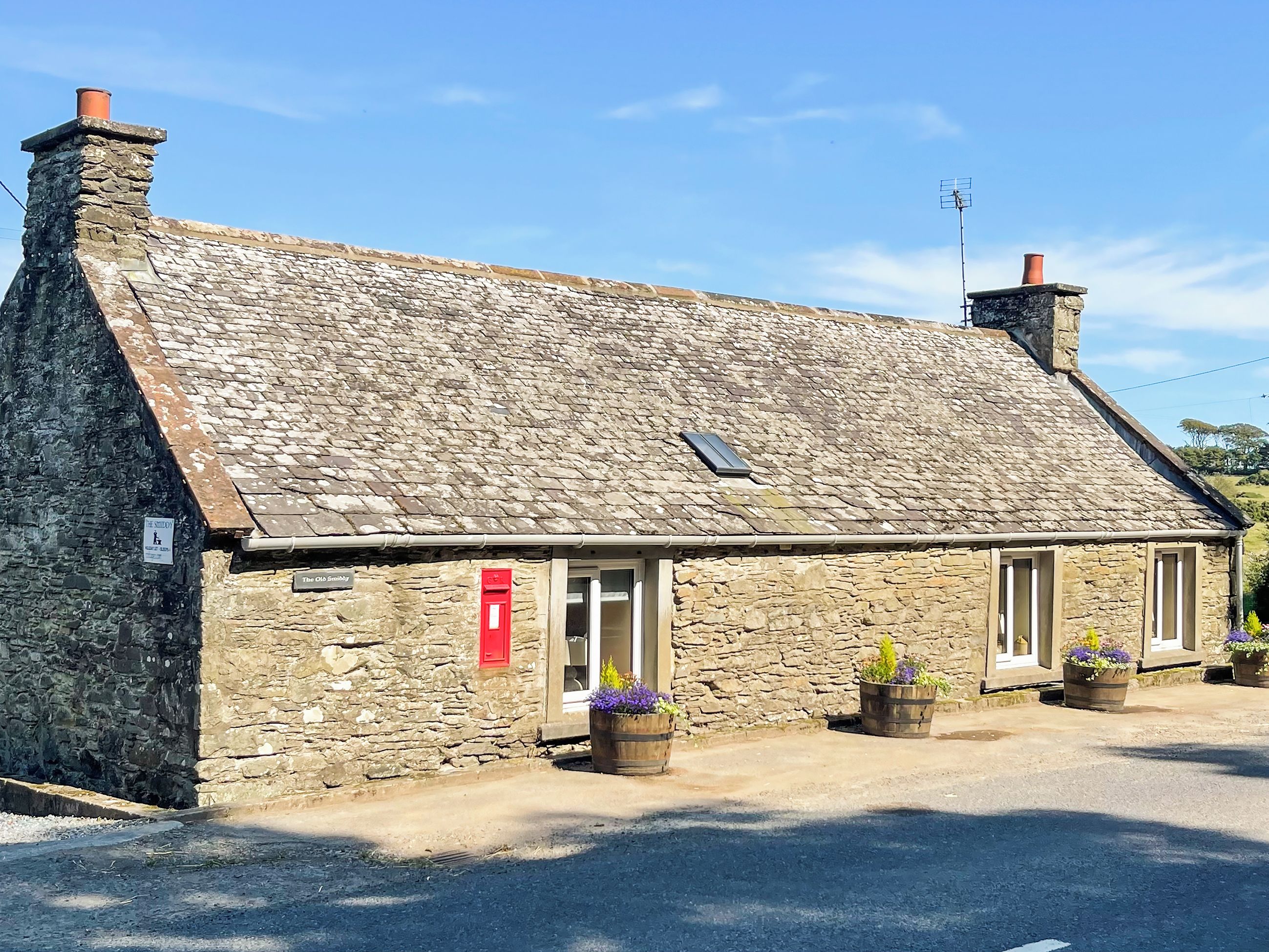 A stone building with a sloped roof, a red mailbox, and potted plants in front.