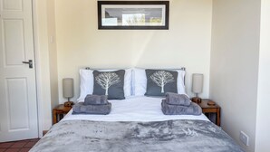 Un letto rifatto con cura, una coperta grigia, due cuscini con motivi alberi e due asciugamani piegati su un lato.