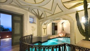 A luxurious indoor pool area with a geometric ceiling design, a large cactus plant, and a well-lit space with a view of the outside. - ANTICO POSITANO - Five Bedroom Villa, Sleeps 9 (Positano)