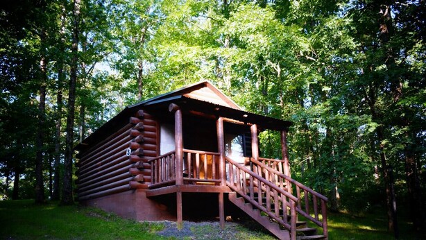 Eine Blockhütte mit einer Holztreppe, die zu einer Veranda führt, umgeben von Bäumen.
