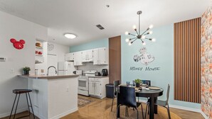 Uma cozinha moderna com armários brancos, uma sala de jantar com mesa redonda e um mural do Mickey Mouse na parede.