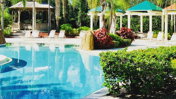 Piscina com espreguiçadeiras e gazebos, cercada por palmeiras e vegetação.