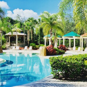 Piscina con sillas de descanso y gazebos rodeados de palmeras y follaje.