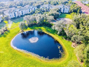 Vista aérea de una zona residencial con un gran estanque, rodeada de céspedes y árboles bien cuidados.
