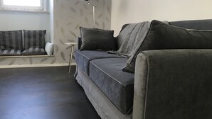 Uma sala de estar moderna com um sofá cinzento, uma mesinha lateral e um abajur.
