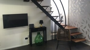 Uma sala de estar moderna com escada preta, uma TV de tela plana, um vaso verde e uma cadeira de vime.