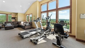 Ein geräumiger Raum mit großem Fenster, Deckenventilator, Laufband, Crosstrainer und einer Couch.