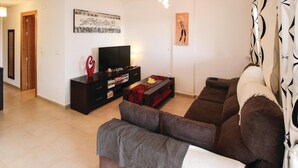 Ein Wohnzimmer mit einem dunklen Holz-Fernsehschrank, einem Flachbildfernseher, einer roten abstrakten Skulptur, einem gemusterten Hocker und einem braunen Sofa.