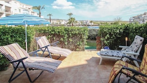 Eine Terrasse im Freien mit vier gestreiften Liegestühlen, einem kleinen Tisch und einem blauen Sonnenschirm.