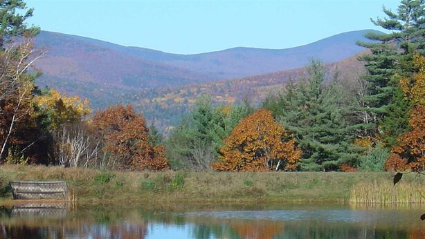 A tranquil lakeside scene with autumn foliage, a bench, and a distant mountain range. - Waterville Estates NH (Campton)