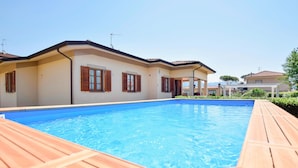 Ein Swimmingpool mit Holzterrasse, ein Haus mit Ziegeldach und klarer Himmel.
