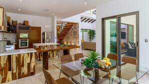 Una cocina moderna con una isla de madera, un comedor con mesa de vidrio y una escalera que sube a un nivel superior.