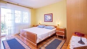 A bedroom with a bed, bedside tables, a nightstand, a window with curtains, a framed picture on the wall, and a small table with a decorative item. - 2 bedroom awesome apartment in Crikvenica (Crikvenica)