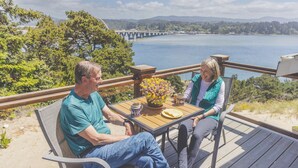 Two people seated at a wooden table with a view of a lake and a bridge in the background. - PUMA POINT...Overlooks the Alsea Bay...Has perfect ocean sunset views! Sleeps 3. (Waldport)