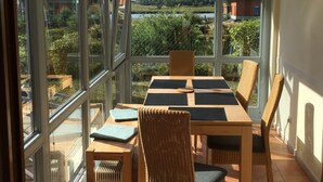 A sunlit dining area with a view of a lake and buildings, featuring a table with chairs and a view through large windows. - 3 bedrooms to 6 people, Sauna, terrace, 4 * equipment, sea view (Sellin)