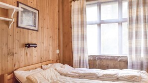 Ett rum med träpanel, en säng, en inramad tavla och ett fönster med gardiner.