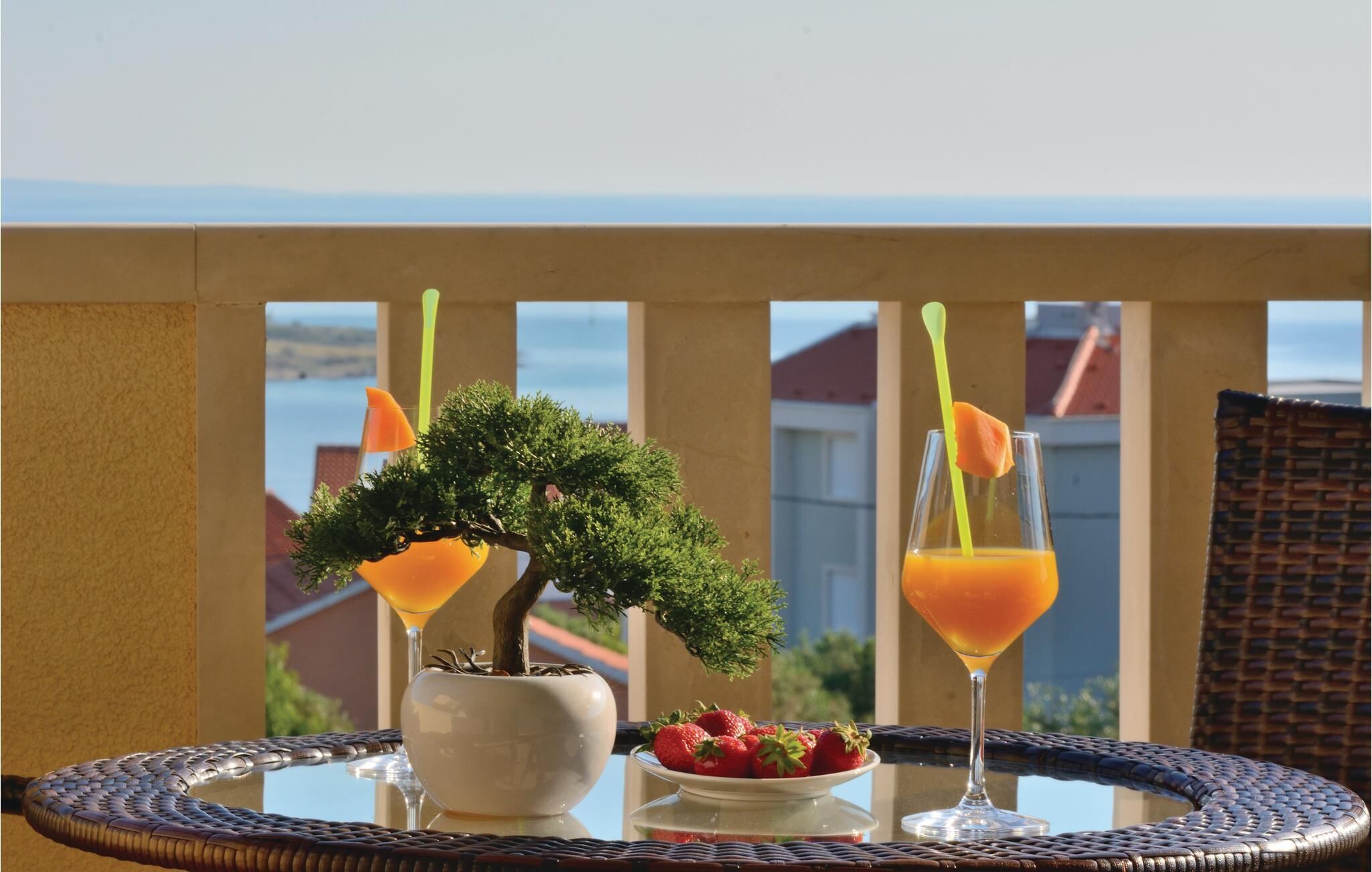 A balcony with a bonsai tree, two drinks with orange liquid, and a plate of strawberries.