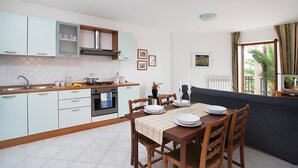 Eine kompakte Küche mit weißen Schränken, ein Esstisch für vier Personen und ein dunkelgraues Sofa im angrenzenden Wohnbereich.