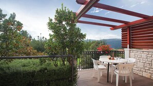 Eine Holzterrasse mit Tisch und Stühlen, umgeben von viel Grün und Blick auf die Berge.