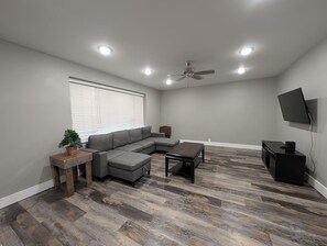 A living room with a sectional sofa, a coffee table, a TV, and a ceiling fan. - Main Street Lodge 2 mins to Downtown Jonesboro and St. Bernards (Jonesboro)