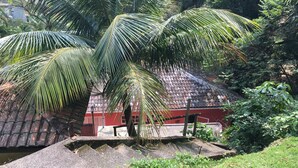 A red building with a tiled roof, surrounded by lush greenery and palm trees. - House 2 suites + 2 apartments - 12 people, Foot of the hill, nature at your window (Praia de Barequecaba)