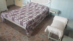 A bedroom with a patterned bedspread, a white upholstered bench, and a small bedside table. - House 2 suites + 2 apartments - 12 people, Foot of the hill, nature at your window (Praia de Barequecaba)
