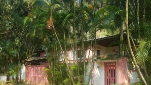 A house surrounded by dense tropical vegetation, with a red gate and a small porch. - House 2 suites + 2 apartments - 12 people, Foot of the hill, nature at your window (Praia de Barequecaba)