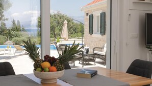 A room with a view of a pool and mountains, a table with a fruit bowl and a book, and a chair. - Luxurious home in Supetar (Supetar)