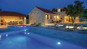 A stone house with a swimming pool, outdoor seating, and a well-lit patio area. - Luxurious home in Supetar (Supetar)