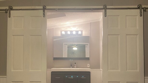 A bathroom with a white vanity, a mirror, and a light fixture above the mirror. - King Size Master With Attached Bath,Pool Table, Open Kitchen,2 Full Baths (Bethel)