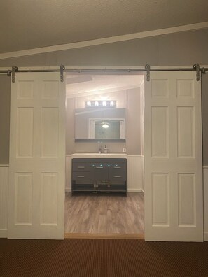 A bathroom with a white vanity, a mirror, and a light fixture above the mirror. - King Size Master With Attached Bath,Pool Table, Open Kitchen,2 Full Baths (Bethel)